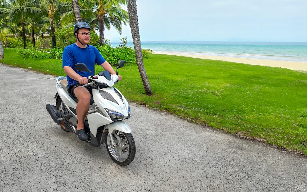Man riding a motorbike along a coastal path in Langkawi.