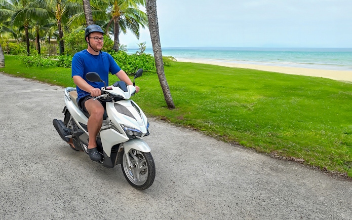 Man riding a motorbike along a coastal path in Langkawi.