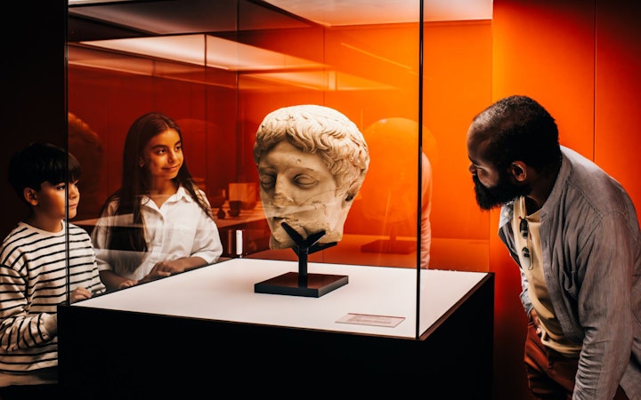 Visitors observing a Roman bust in a museum exhibit on Pompeii.