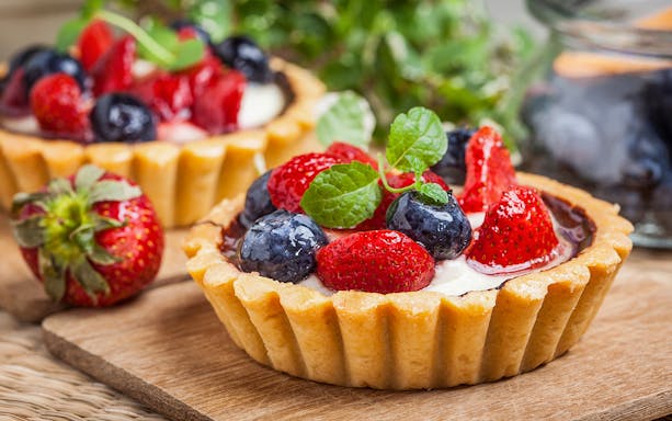 Berry tarts with strawberries and blueberries on a wooden board, Paris Saint Germain food tour.