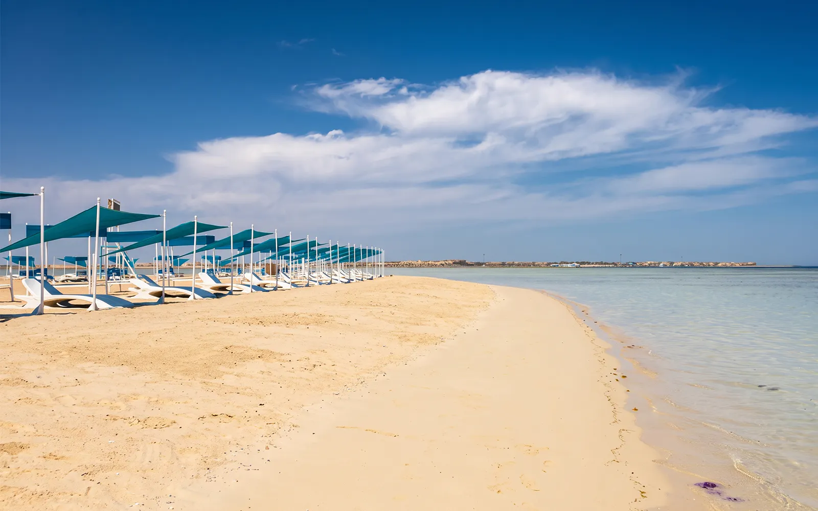 Sandy beach with sunshades on Bianca Island, Hurghada, near clear blue water.