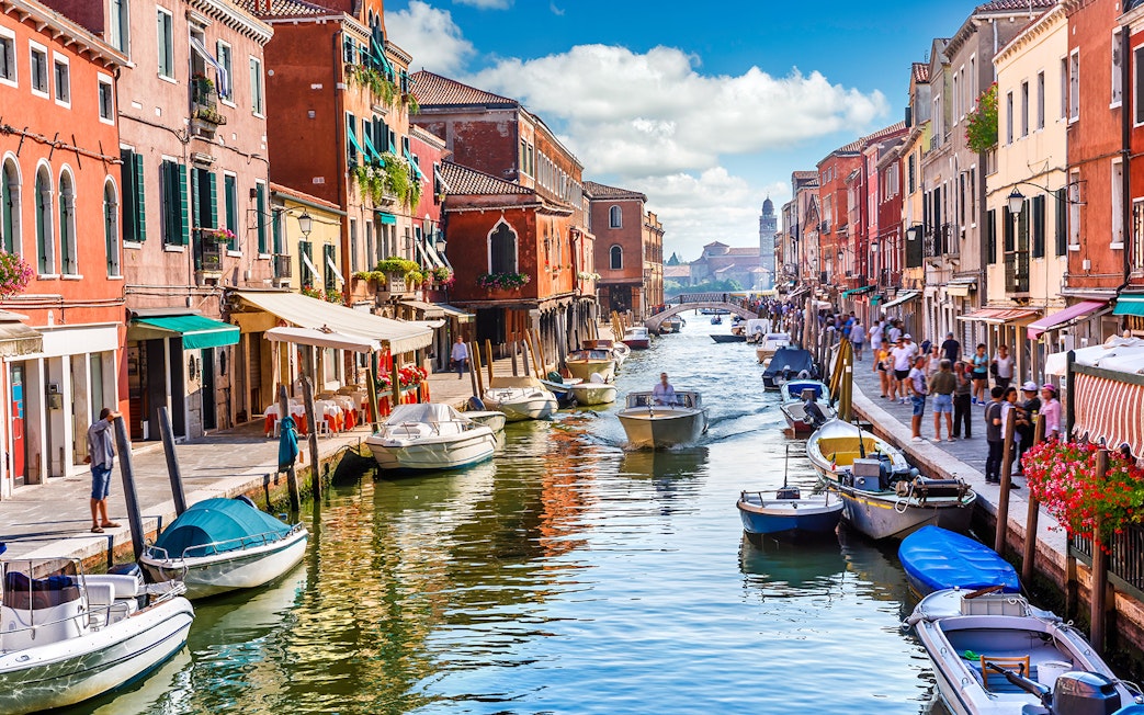 Canal with boats and colorful buildings on Murano Island, Venice, during a guided tour.