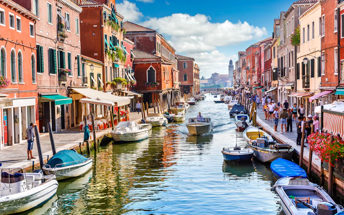 Canal with boats and colorful buildings on Murano Island, Venice, during a guided tour.