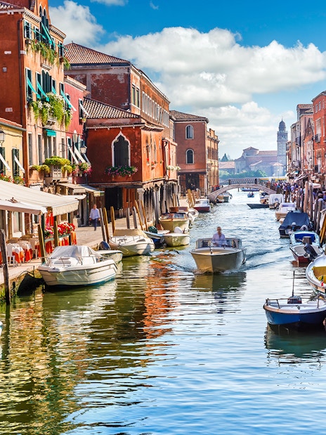 Canal with boats and colorful buildings on Murano Island, Venice, during a guided tour.