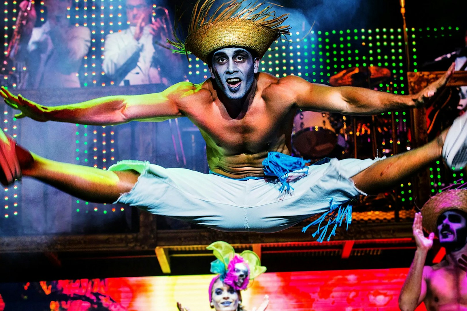 Performer in mid-air split during Zombie Burlesque show with vibrant stage lights.