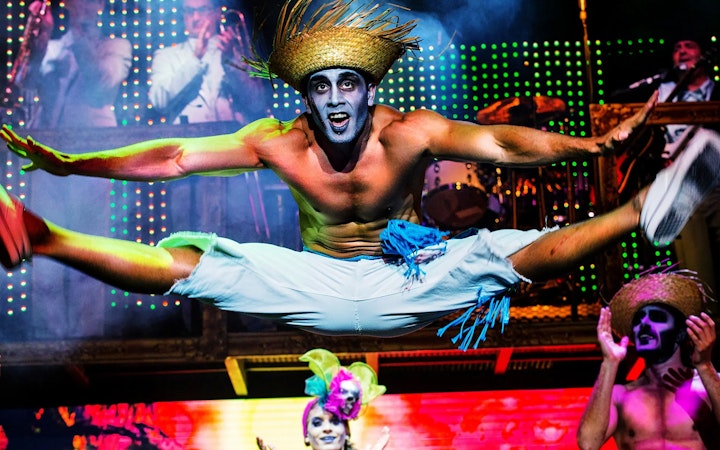 Performer in mid-air split during Zombie Burlesque show with vibrant stage lights.