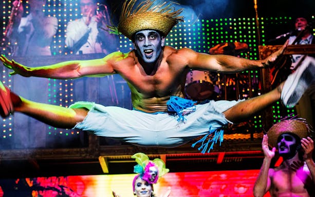 Performer in mid-air split during Zombie Burlesque show with vibrant stage lights.