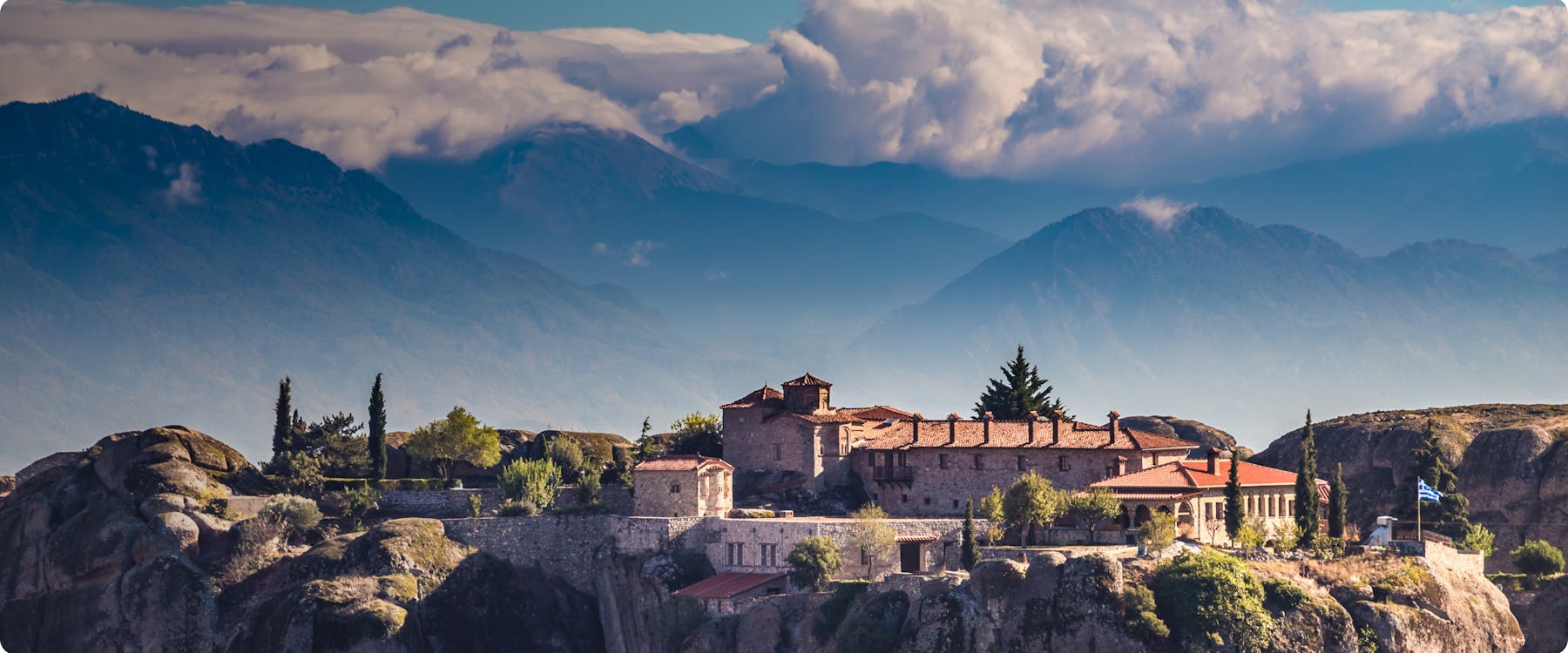Monastery on rock formations in Meteora, Greece, with mountains in the background.
