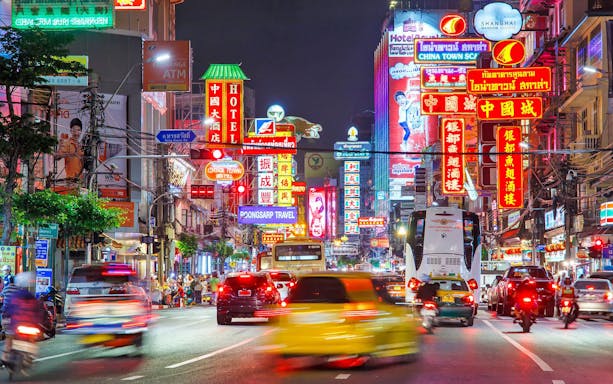 Bangkok Chinatown street with neon signs and bustling traffic at night.