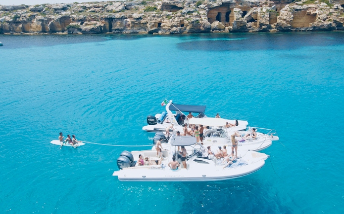 Boat tour with people enjoying the sea near rocky coastline of Favignana and Levanzo.