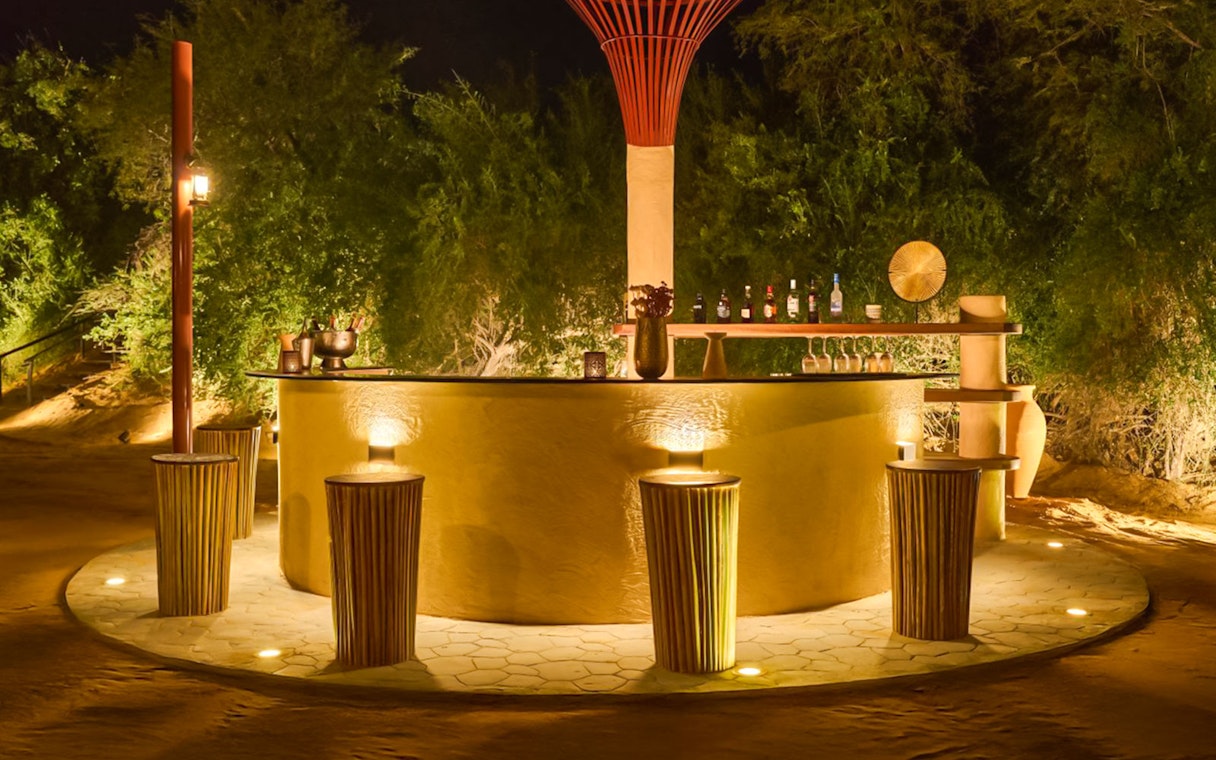 Bar counter at The Nomad Garden, a premium desert dining experience, with stools and ambient lighting.