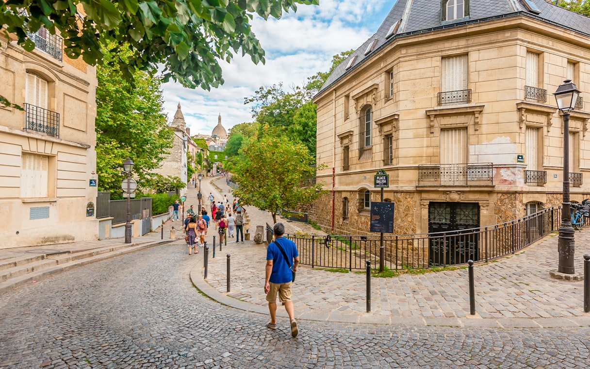 Tourists walking on cobblestone streets in Montmartre, Paris with historic buildings.