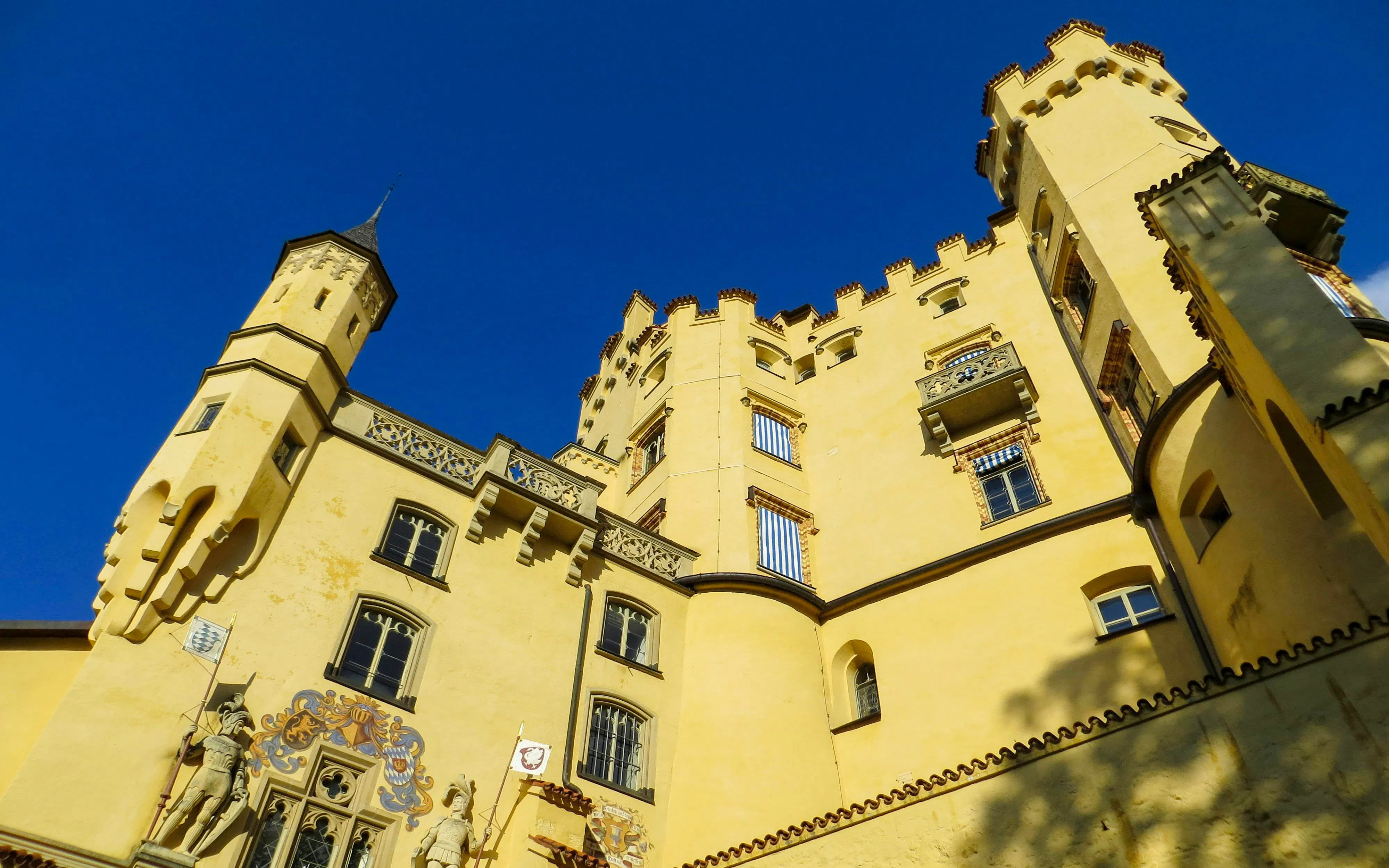Hohenschwangau Castle facade with towers under clear blue sky, Bavaria.