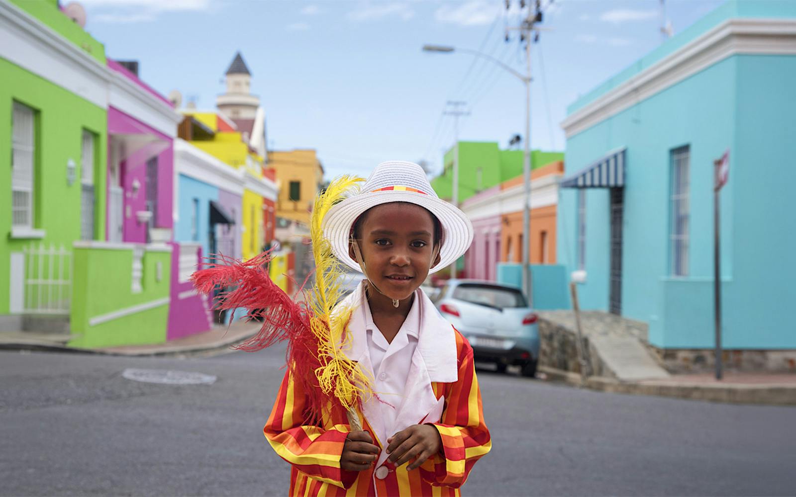 Child in colorful attire in Bo-Kaap, Cape Town, with vibrant houses in the background.