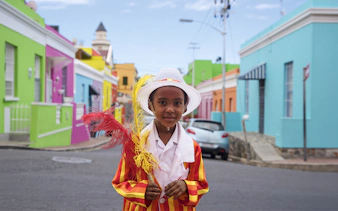 Child in colorful attire in Bo-Kaap, Cape Town, with vibrant houses in the background.