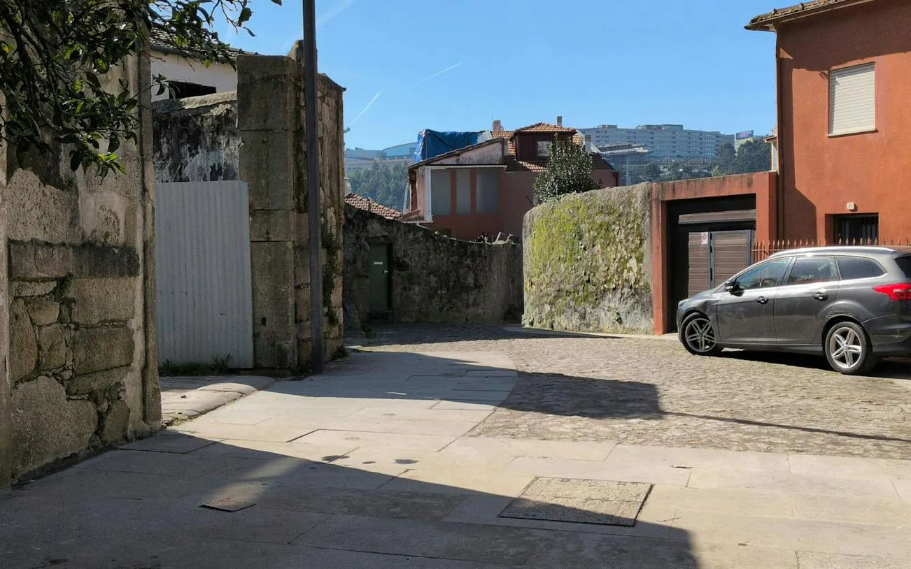Narrow cobblestone street in Porto with stone walls and parked car, part of self-guided city exploration game.
