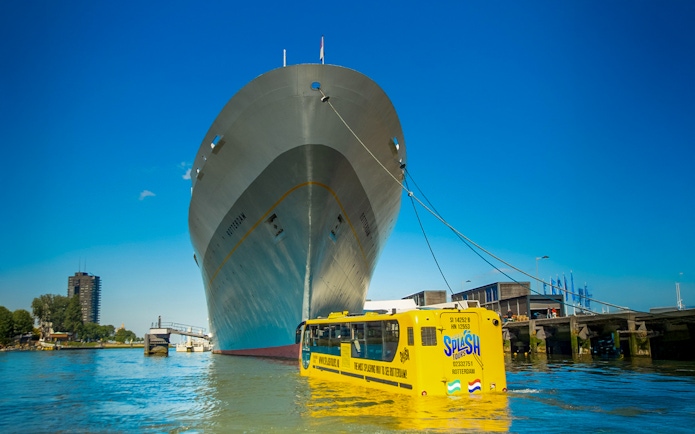 Amphibious bus on Rotterdam waterway near large ship during 1-hour sightseeing splash tour.