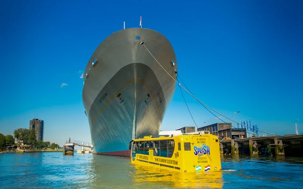 Amphibious bus on Rotterdam waterway near large ship during 1-hour sightseeing splash tour.