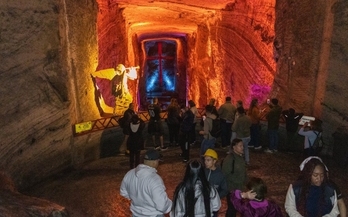 Tourists exploring the illuminated Zipaquira Salt Cathedral with angel statue and cross.