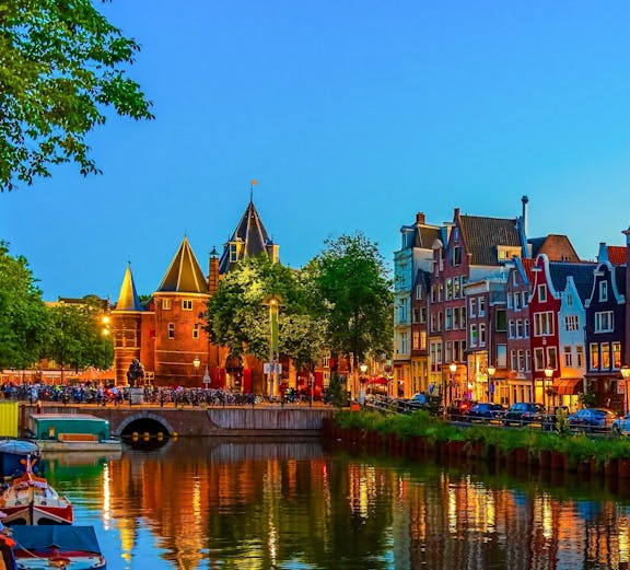 Canal view of De Wallen at night, Amsterdam, with illuminated buildings reflecting in water.