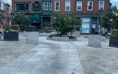 Urban square with planters and historic buildings in Boston, part of a self-guided city exploration game.