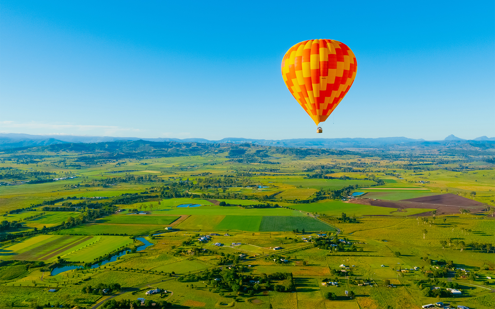 Hot air balloon over Gold Coast countryside, Australia, with fields and distant mountains.