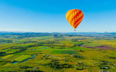 Hot air balloon over Gold Coast countryside, Australia, with fields and distant mountains.