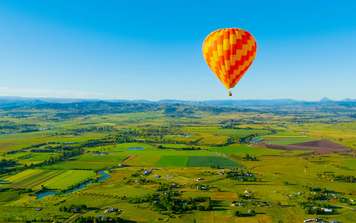 Hot air balloon over Gold Coast countryside, Australia, with fields and distant mountains.
