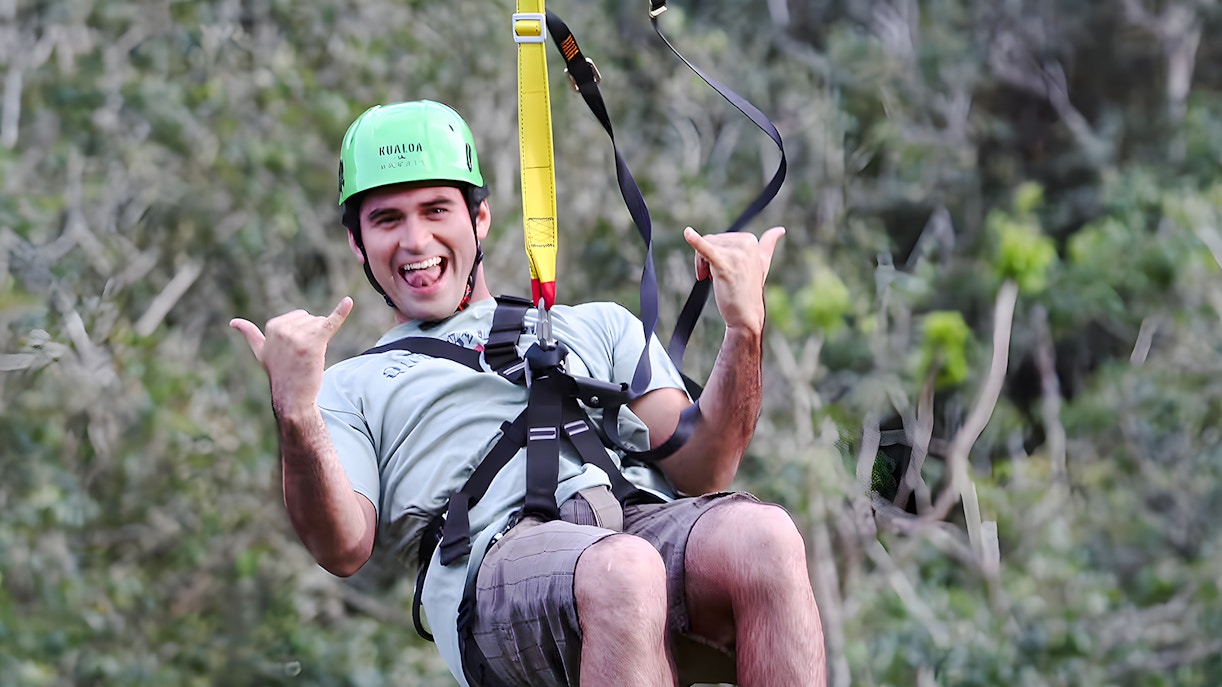 Person ziplining at Kualoa Ranch, Hawaii amidst lush greenery.
