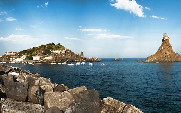 Riviera of the Cyclops coastline with rocky formations and boats near Catania, Sicily.