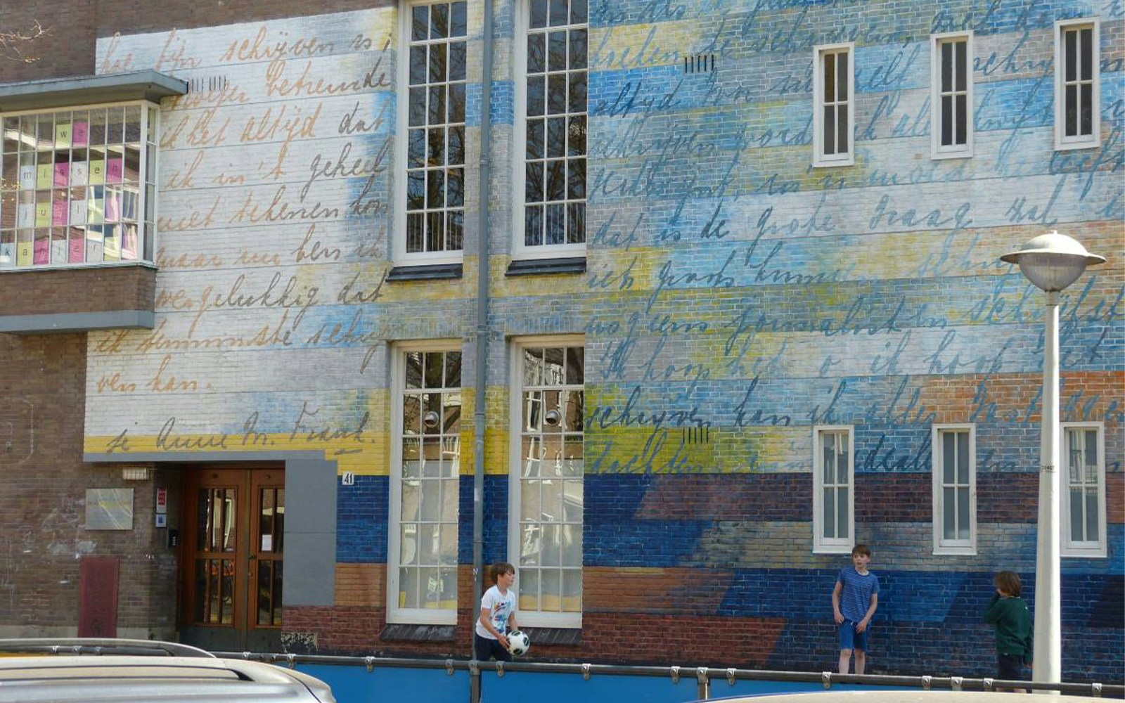 Colorful mural with handwritten text on a building wall in Amsterdam neighborhood.
