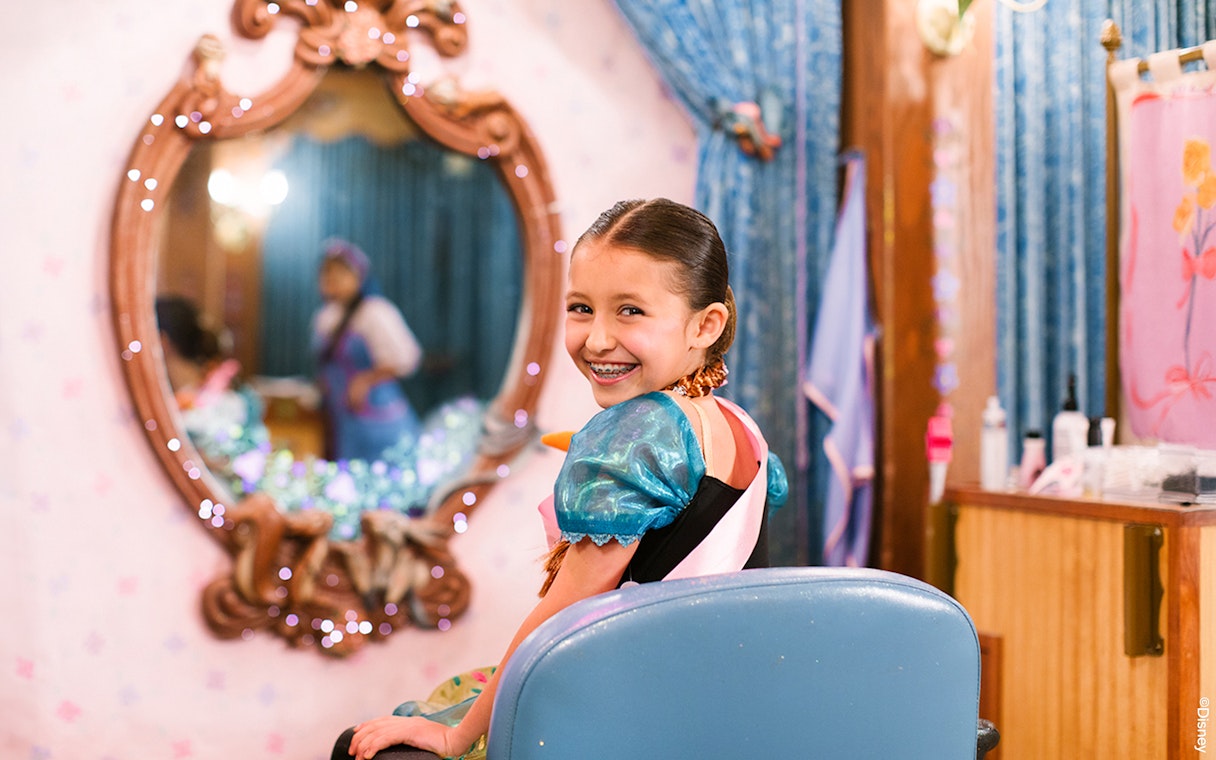 Child in costume smiling at Disneyland Park, California, with a mirror reflection.