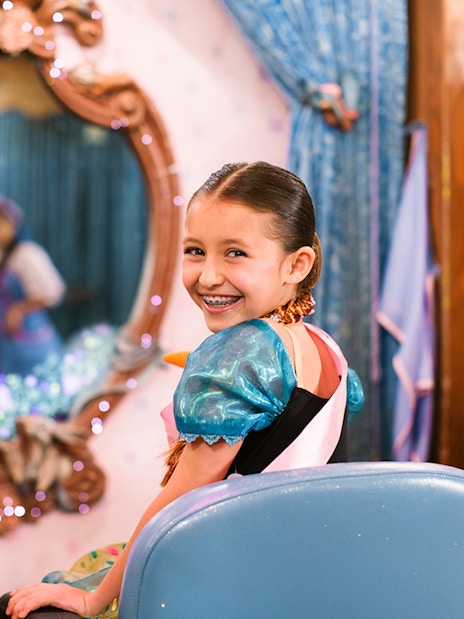 Child in costume smiling at Disneyland Park, California, with a mirror reflection.