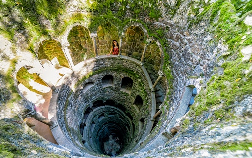 Initiation Well at Quinta da Regaleira, Sintra, Portugal with spiral staircase and moss-covered walls.