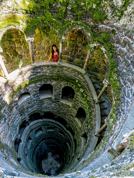 Initiation Well at Quinta da Regaleira, Sintra, Portugal with spiral staircase and moss-covered walls.