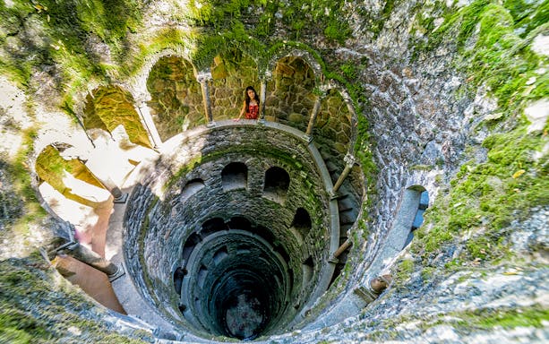 Initiation Well at Quinta da Regaleira, Sintra, Portugal with spiral staircase and moss-covered walls.