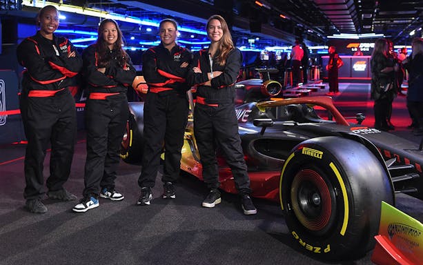 Four people in racing suits stand beside an F1 car at the F1® Drive London event.