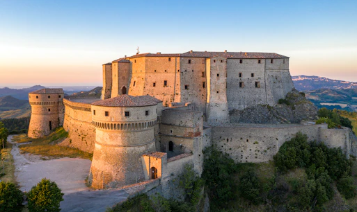 San Leo Fortress in Rimini, Italy, at sunset with surrounding hills.