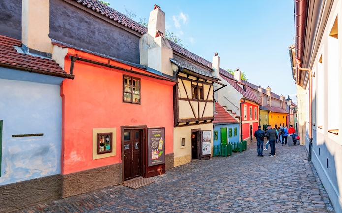 Colorful historic houses on Golden Lane, Prague, with tourists walking along the cobblestone street.