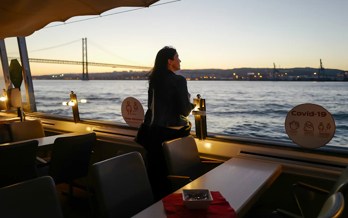 Person enjoying sunset view on Tagus River cruise in Lisbon with bridge in background.