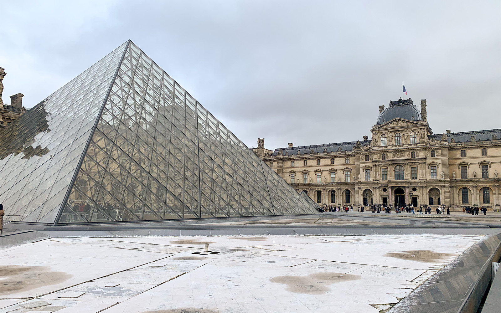 Grupo de visitantes del Museo del Louvre explorando la icónica entrada de la pirámide de cristal en París, Francia.