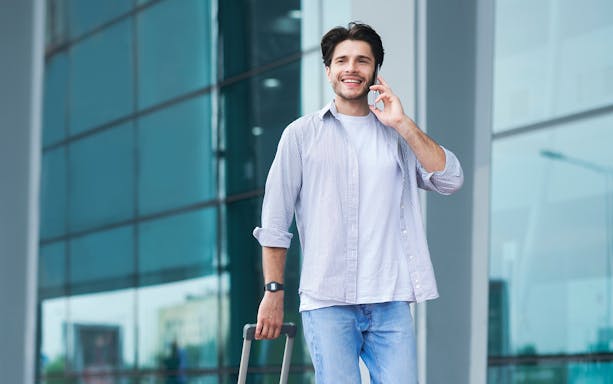 Traveler using phone at Kota Kinabalu Airport with luggage, Malaysia 4G SIM card.