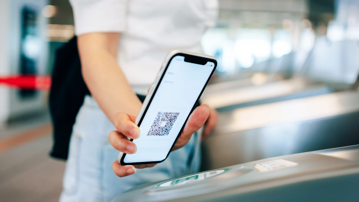 Young woman scanning QR code at subway turnstile with smartphone for contactless payment.