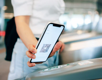 Young woman scanning QR code at subway turnstile with smartphone for contactless payment.