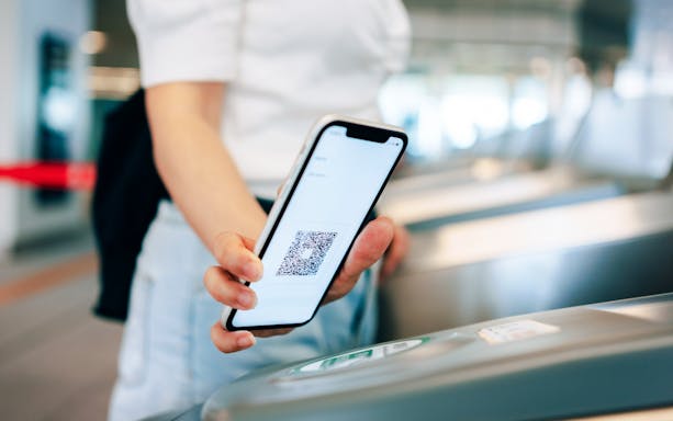Young woman scanning QR code at subway turnstile with smartphone for contactless payment.
