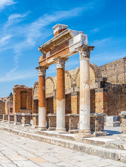 Ancient Roman columns and ruins in Pompeii, Naples under a clear blue sky.