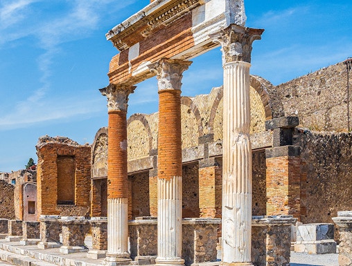 Ancient Roman columns and ruins in Pompeii, Naples under a clear blue sky.