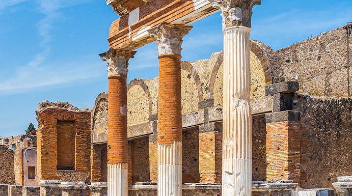 Ancient Roman columns and ruins in Pompeii, Naples under a clear blue sky.