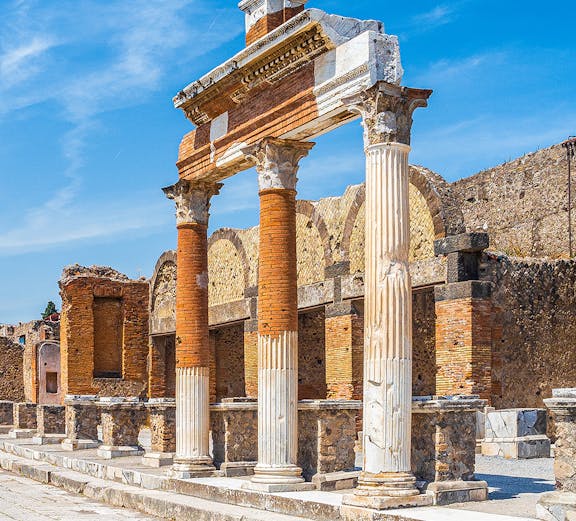 Ancient Roman columns and ruins in Pompeii, Naples under a clear blue sky.
