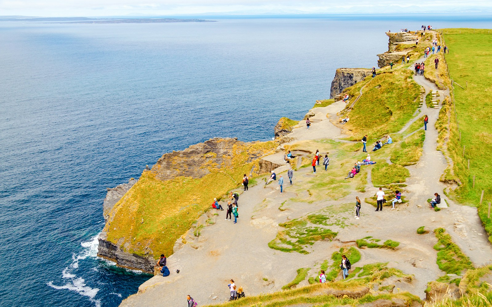 Visitors walking along the Cliffs of Moher, Ireland, with ocean views.